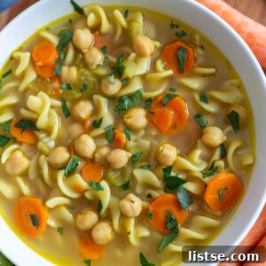 A close-up of a bowl of chickpea noodle soup, garnished with fresh herbs, ready to be enjoyed.