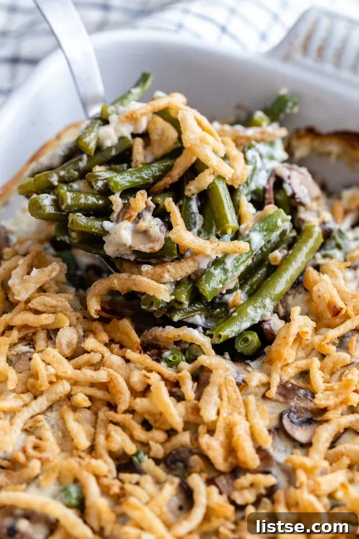 Classic green bean casserole in a baking dish, beautifully topped with golden-brown fried onions, with a serving spoon taking a portion out.