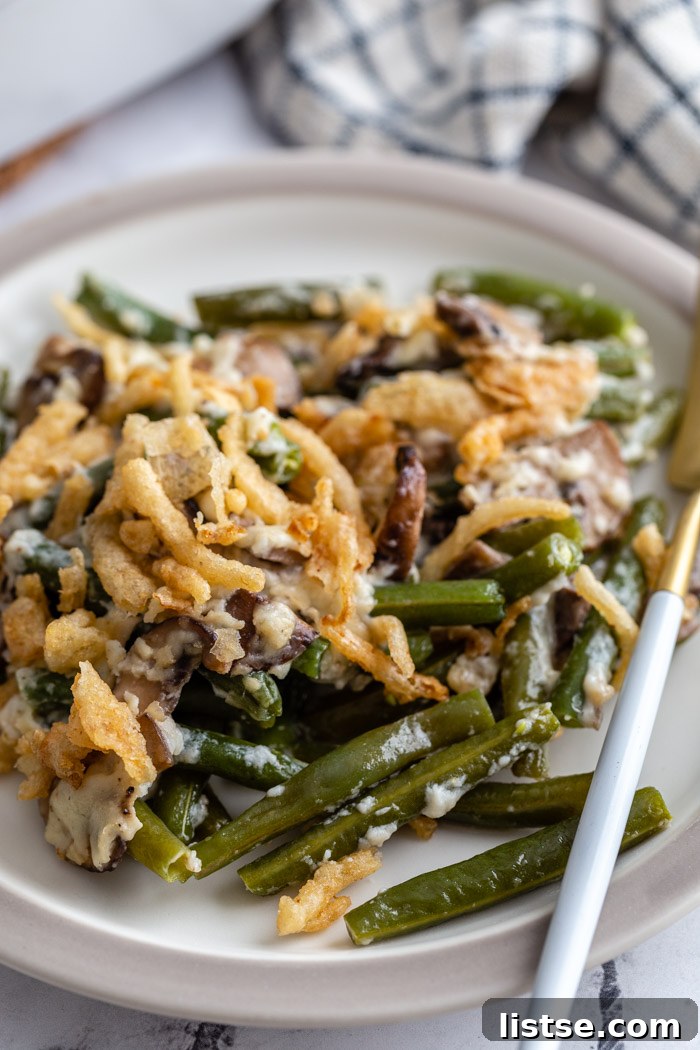 A close-up shot of vegan green bean casserole on a white plate, adorned with a generous sprinkle of golden-crisp fried onions.