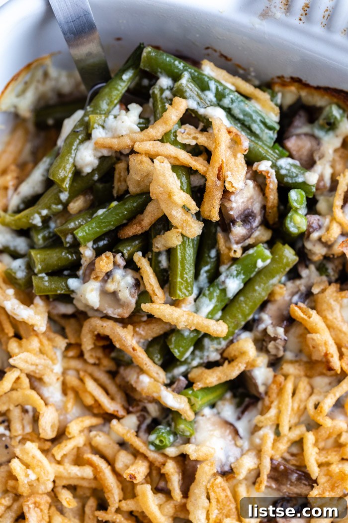 A close-up of a baking dish filled with homemade vegan green bean casserole, generously topped with golden fried onions.