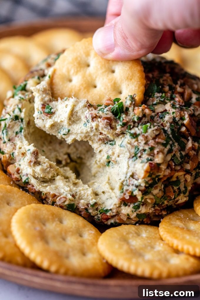 A crisp Ritz cracker being dipped into the creamy vegan cheese ball, showing off its inviting texture.