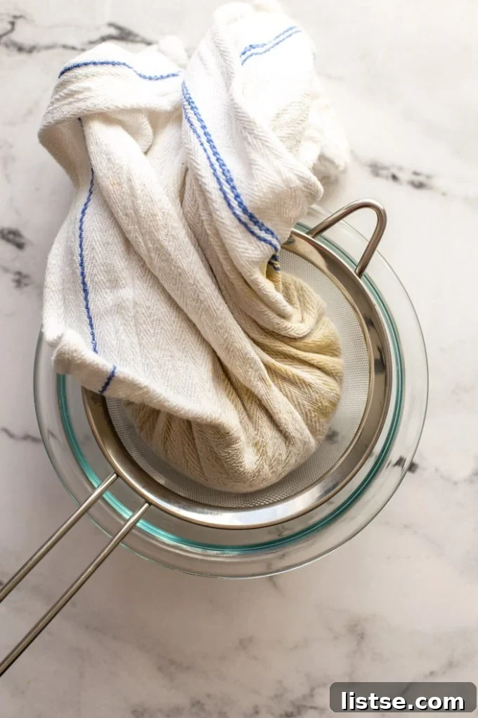The smooth cashew mixture being poured into the center of a cheesecloth, ready to be formed into a ball.