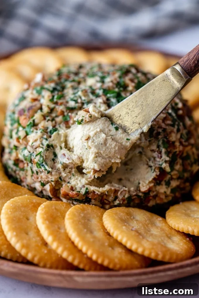 A cheese spreader gracefully dipping into the creamy vegan cheeseball, highlighting its smooth and inviting texture.