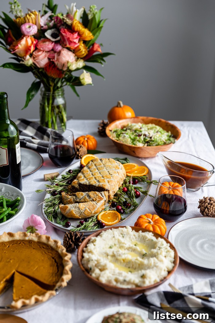 thanksgiving table with flowers on it, side dishes, and a sliced wellington
