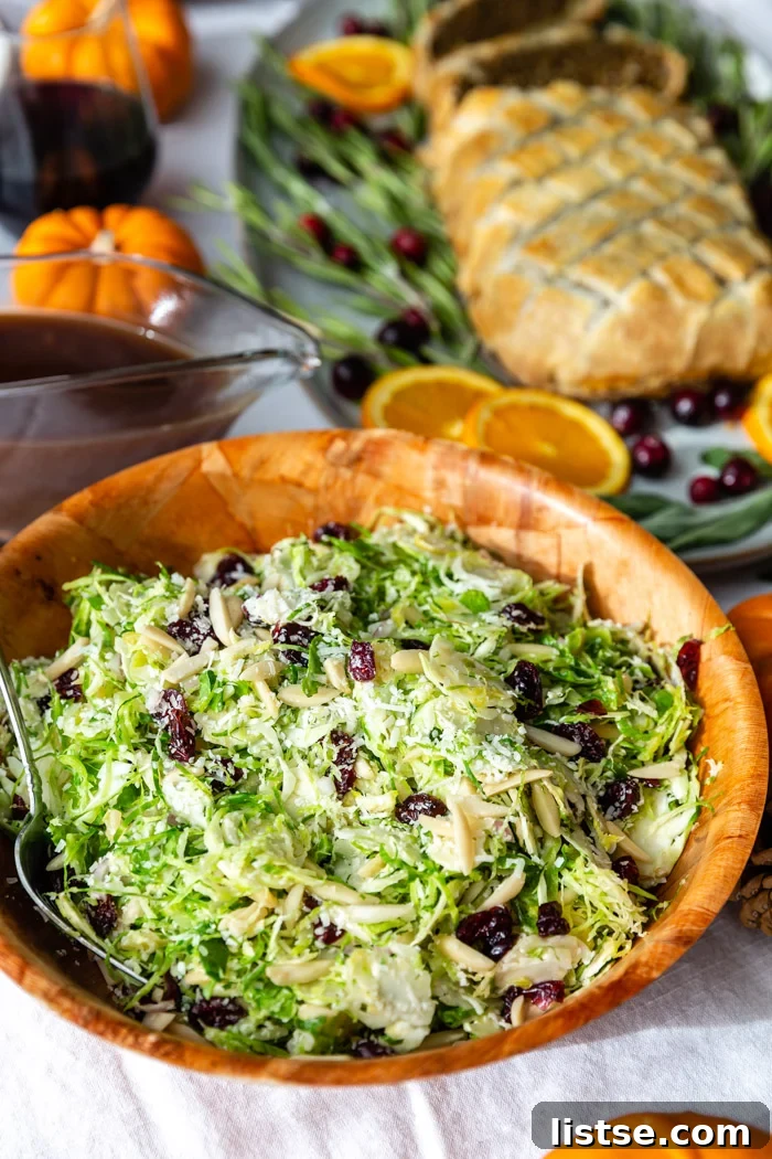 bowl of brussels sprouts salad on a thanksgiving table with a wellington in the background