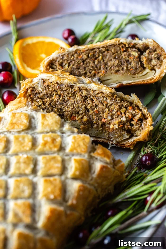 A magnificent vegetarian Wellington proudly displayed on a large festive platter, artfully adorned with fresh rosemary, bright orange slices, and glistening fresh cranberries. Several slices have been removed, showcasing its appealing layers.