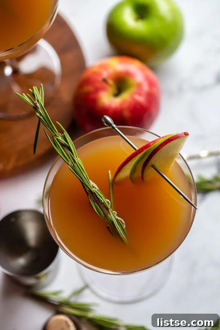 apple cider cocktail in a cocktail glass garnished with apple slices and rosemary and apples in the background
