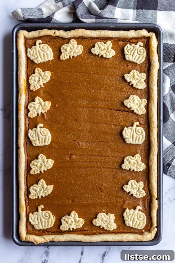 Pumpkin Slab Pie 4 sheet pan pumpkin pie laying on top of a checkered towel. the pie is framed by little pumpkin and leaf pie crust cutouts
