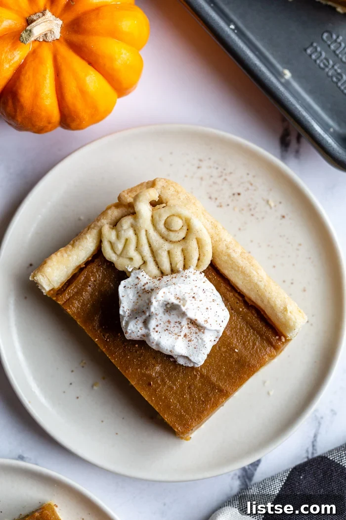 Pumpkin Slab Pie 6 square slice of pumpkin pie topped with a pie crust pumpkin and whipped cream. a small orange pumpkin in the corner of the shot