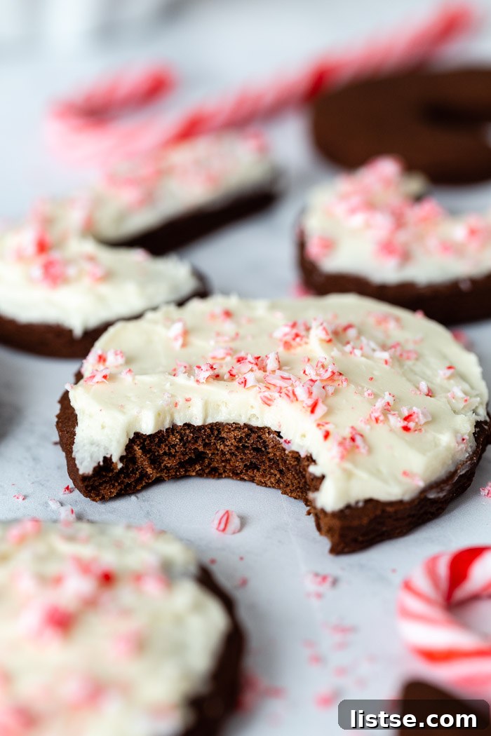 up close shot of a round chocolate sugar cookie that's topped with vanilla frosting and crushed peppermint. more cookies in the background