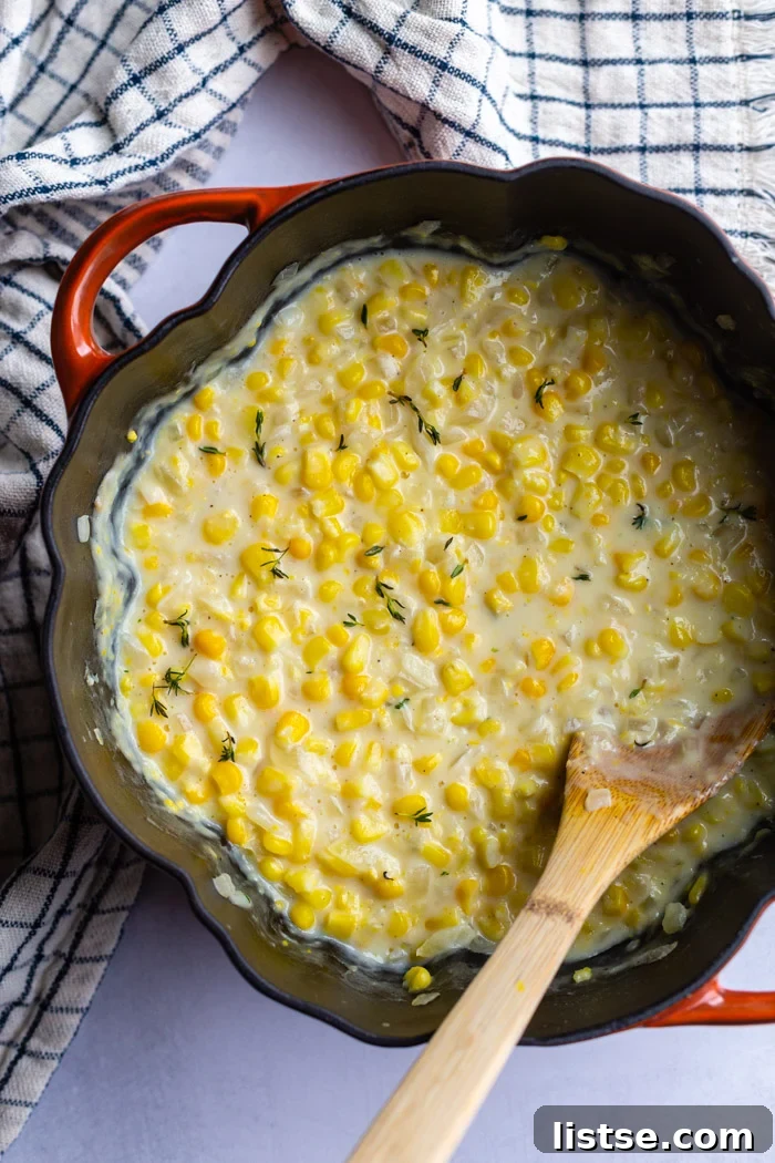 Velvety Vegan Creamed Corn 2 Large cast iron pot filled with luscious vegan creamed corn, garnished with fresh thyme. A wooden spoon rests on the side, inviting a taste.