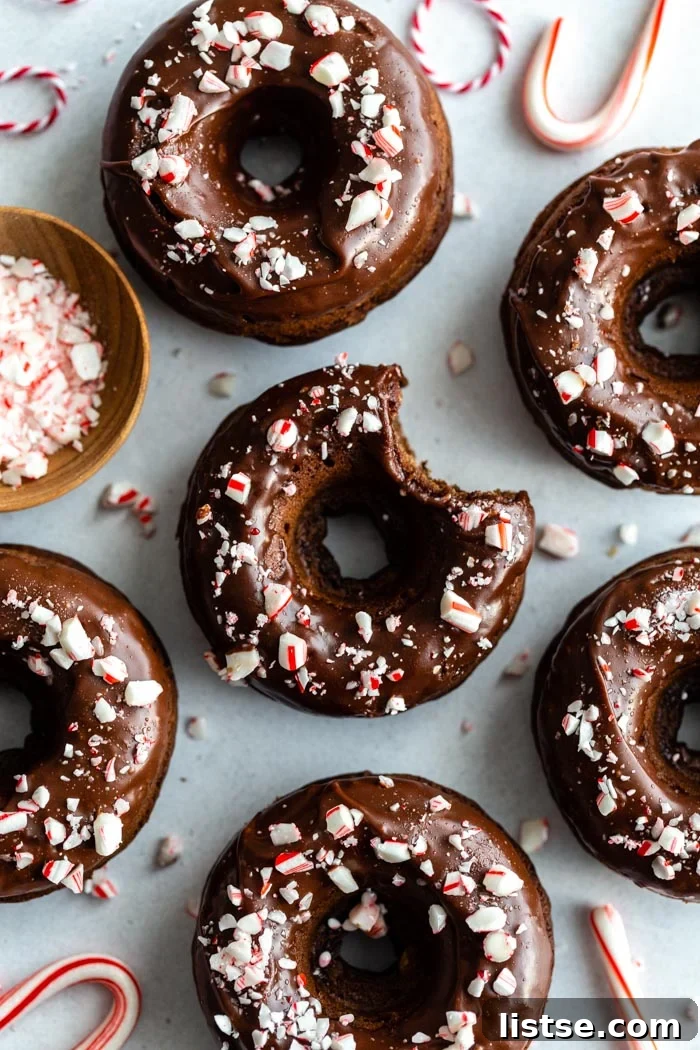 A stunning spread of vegan baked chocolate peppermint donuts, glistening with glaze and sprinkled with crushed candy canes, ready to be enjoyed.