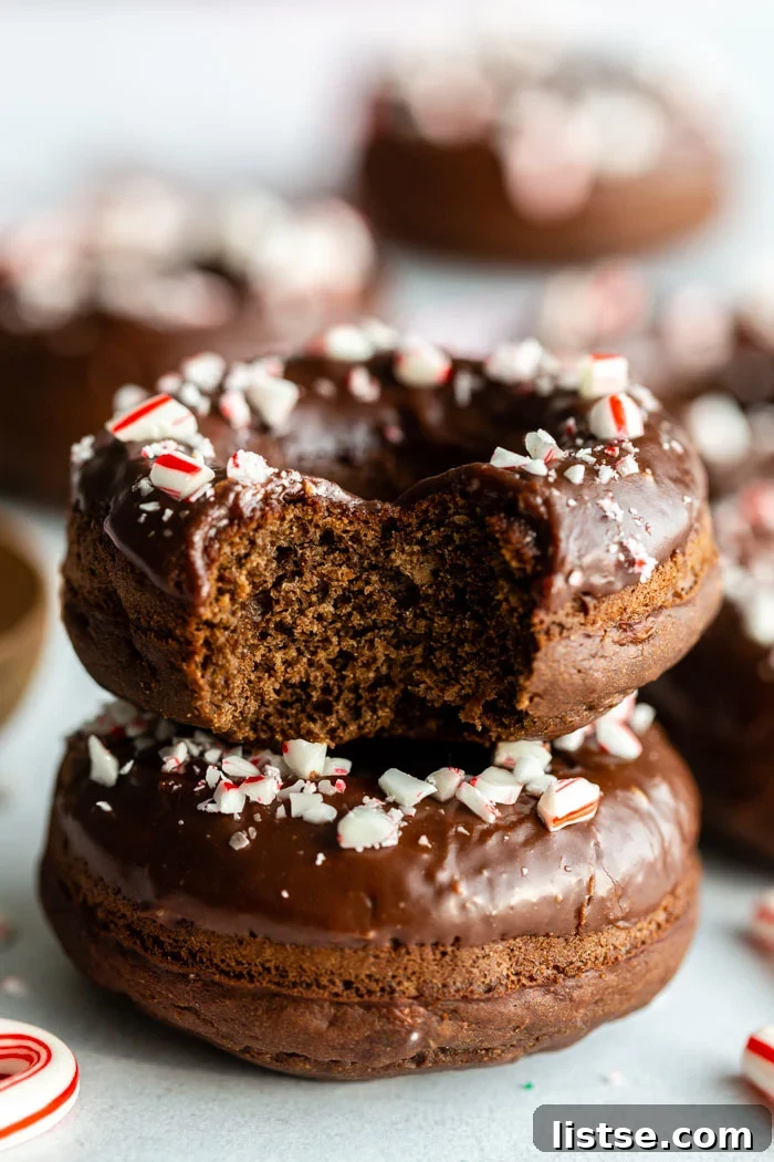 A stack of chocolate peppermint donuts, one with a bite taken out, revealing the moist interior and rich chocolate glaze with crushed peppermint.