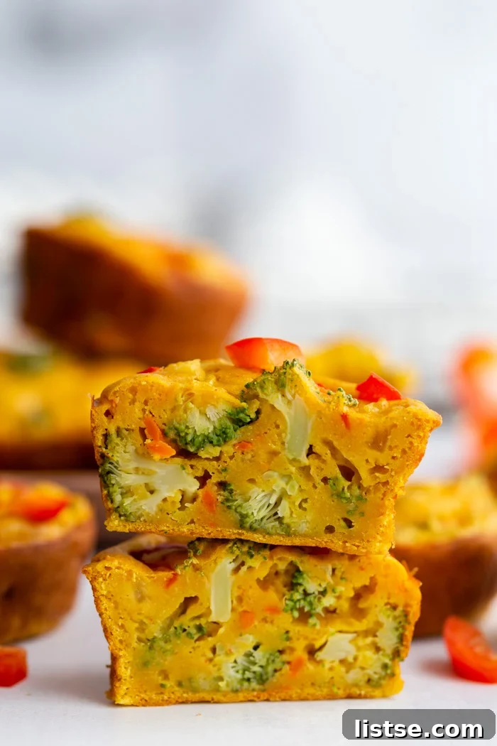 A beautifully presented vegan egg cup, expertly cut in half and stacked, revealing its hearty interior filled with colorful vegetables. More vegan egg cups are blurred in the background, creating an inviting scene.