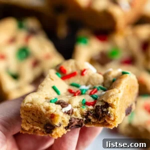 hand holding up a chocolate chip cookie bar that has red white and green sprinkles on top. more cookie bars in the background