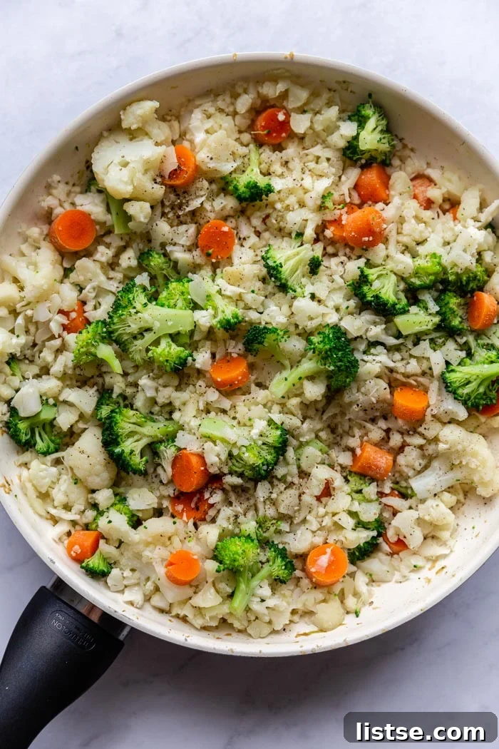 Skillet filled with vibrant cauliflower fried rice, featuring broccoli florets and shredded carrots, ready to be served.