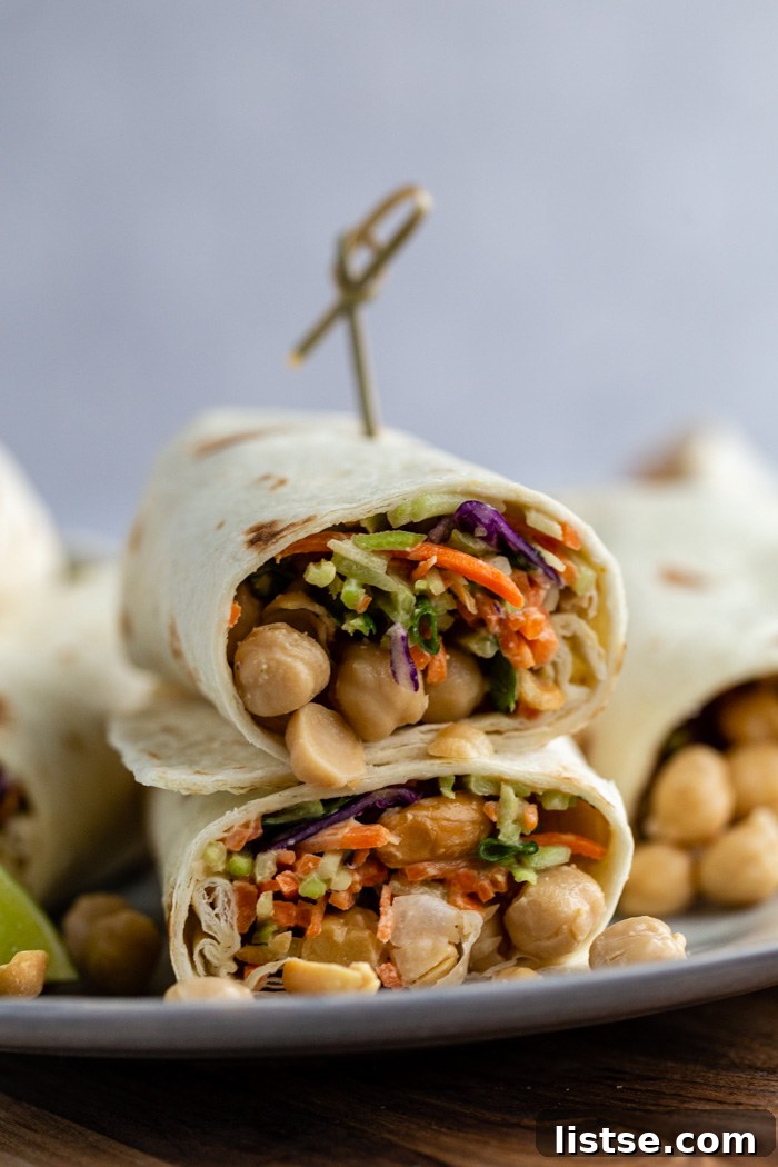 Savory Peanut Chickpea Wraps 3 A close-up of a halved chickpea tortilla wrap, revealing a colorful interior of veggie slaw, whole chickpeas, and a rich peanut sauce, neatly stacked.