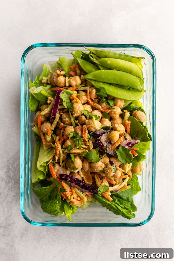 Savory Peanut Chickpea Wraps 6 A meal prep container showcasing a bed of lettuce topped with a chickpea and coleslaw mix, alongside fresh sugar snap peas, ready for a healthy lunch.