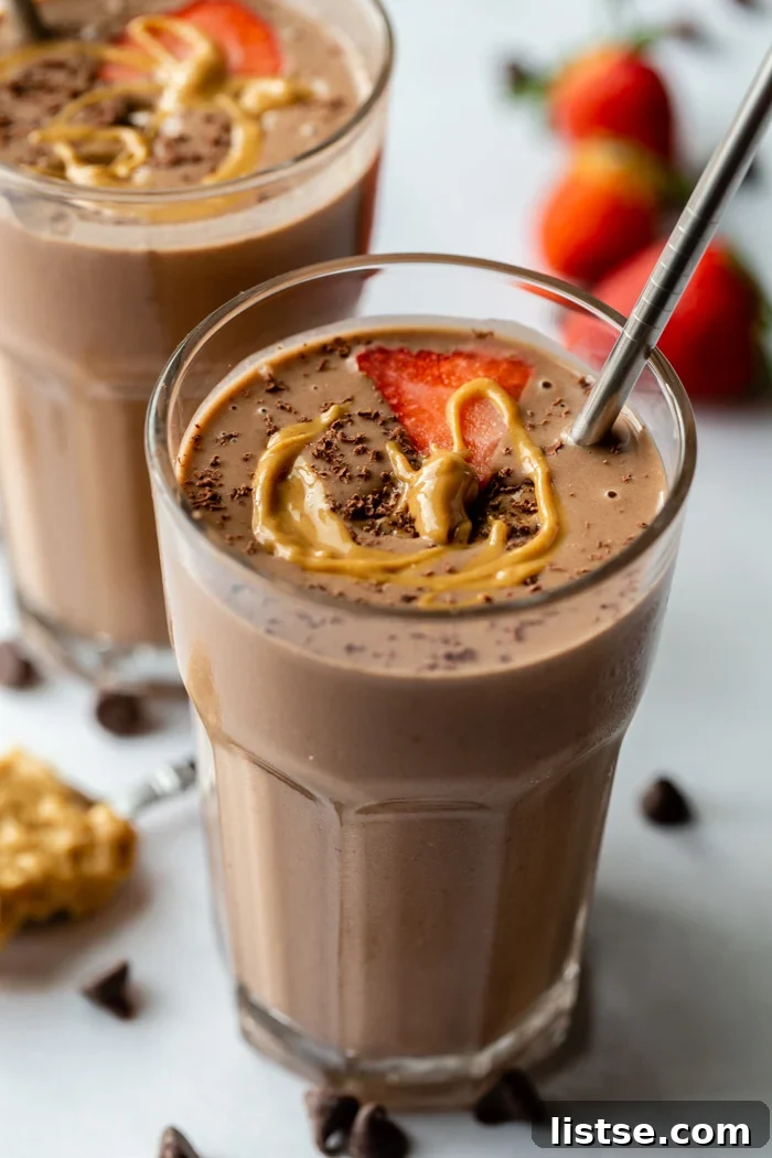 Close-up of two elegantly presented chocolate peanut butter smoothies, adorned with fresh strawberry, chocolate shavings, and a swirl of peanut butter