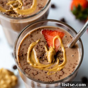 Two glasses filled with a chocolate peanut butter smoothie and topped with a slice of strawberry, shredded chocolate and a drizzle of peanut butter