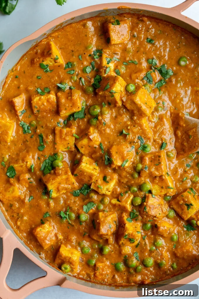 Close-up of Tofu Tikka Masala being cooked in a large pink skillet, highlighting the delicious sauce and tofu pieces