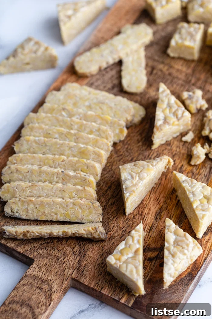 tempeh on a wood cutting board cut in several different ways including slices, cubed, and triangles