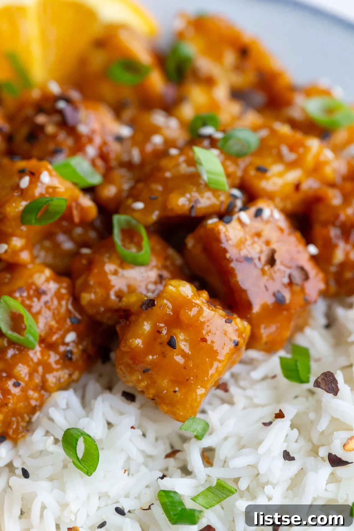 A vibrant plate of orange tofu, rice, and fresh orange slices, ready to be enjoyed.