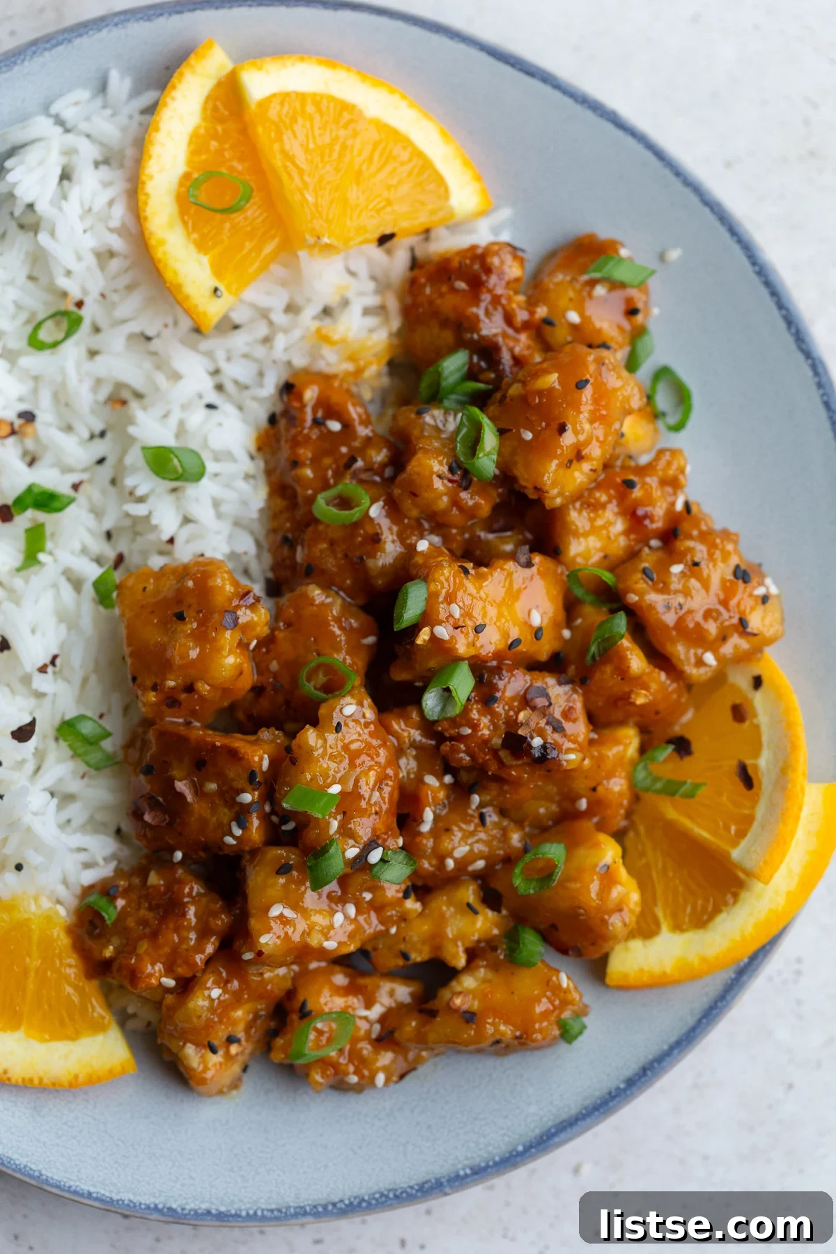 A delicious serving of orange tofu with rice and garnished with orange slices and green onions.