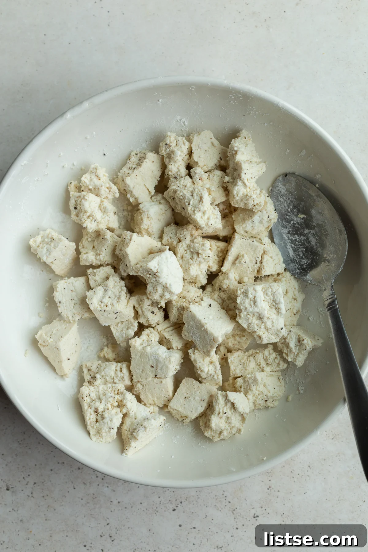 Tofu chunks evenly coated with cornstarch, salt, and pepper in a bowl.