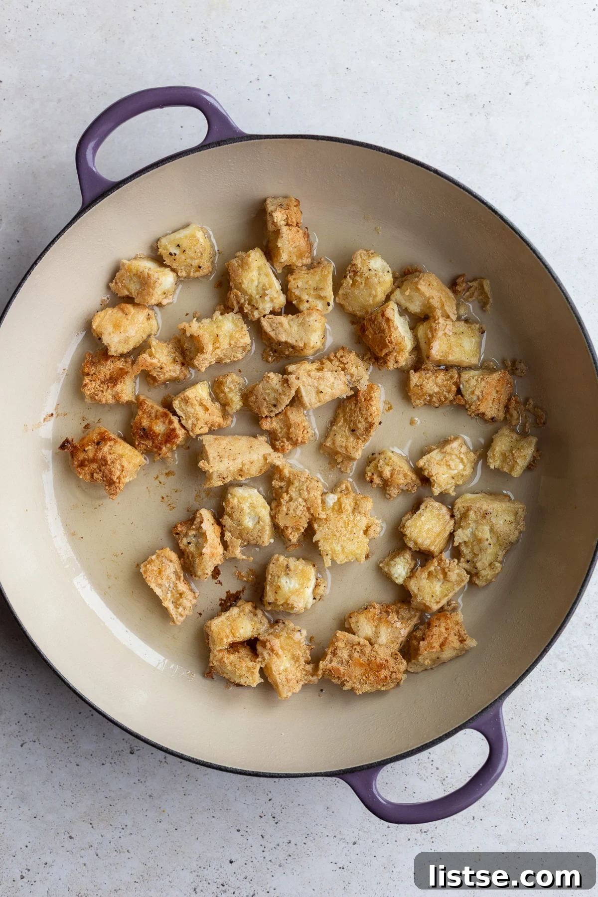 Crispy golden-brown tofu frying in a large skillet until perfectly browned.