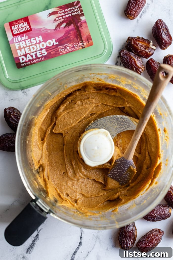Natural Date Sweetener 7 Creamy date paste glistening in the bowl of a food processor, surrounded by a scatter of fresh whole dates.