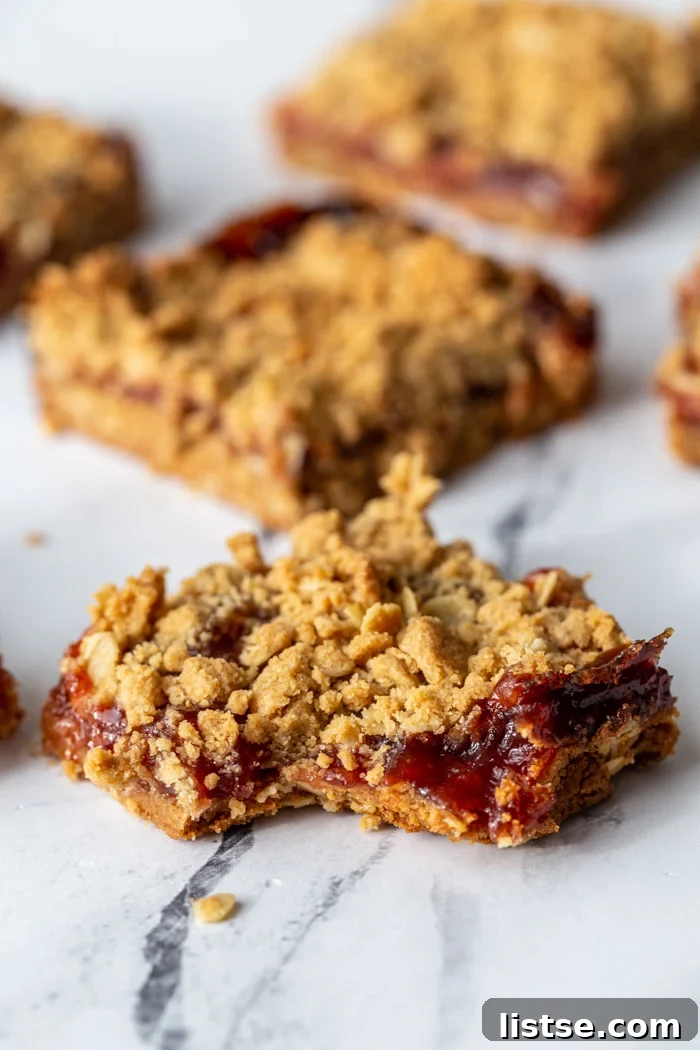 Close-up of a peanut butter and jelly crumble bar with a bite taken out, revealing the soft peanut butter crust and vibrant jelly filling.
