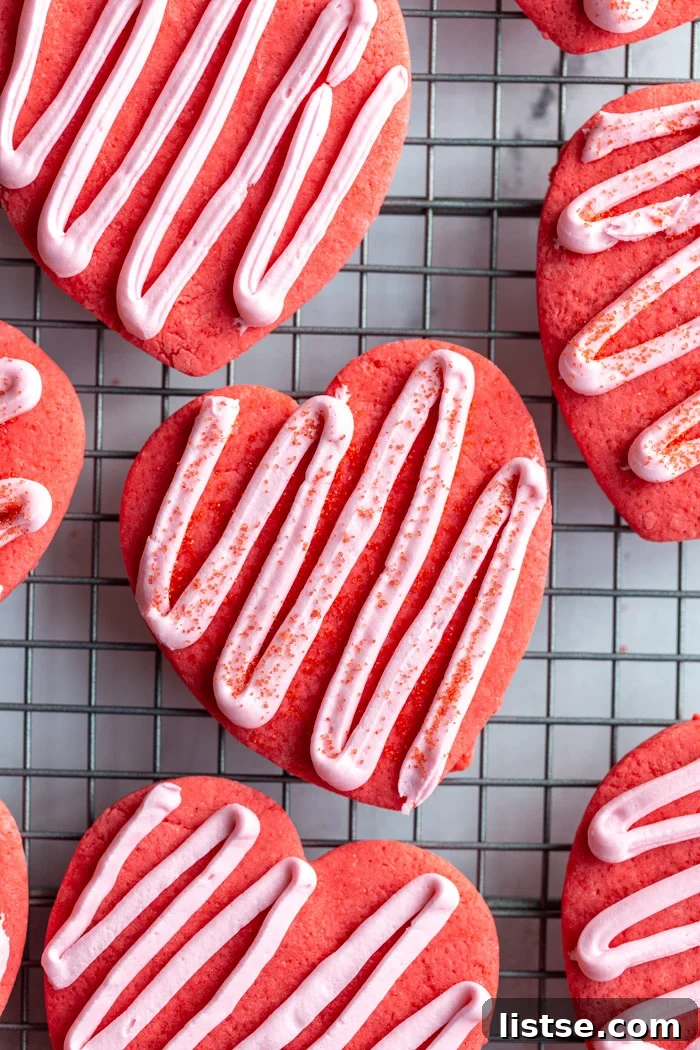 Vibrant red heart-shaped vegan sugar cookies with delicate pink zig-zag frosting resting on a cooling rack, perfect for Valentine's Day.