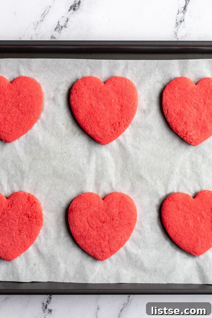 Batch of freshly baked red heart-shaped vegan sugar cookies, ready for frosting and celebrating Valentine's Day.