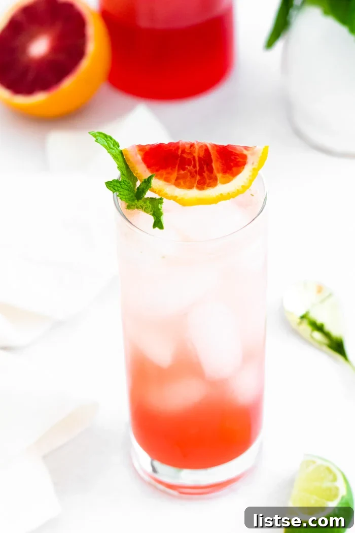 Ruby Red Mojito 5 Tall glass filled with ice and a blood orange mojito and blood orange slice and mint on the top. blood orange in the background