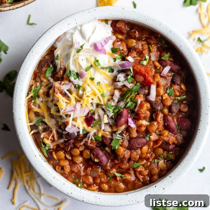 A vibrant bowl of lentil chili, generously topped with dairy-free sour cream, shredded vegan cheese, and fresh cilantro, ready to be enjoyed.