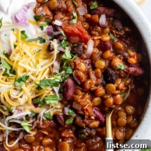 Lentil chili topped with cheese, sour cream, and fresh cilantro, presented in a bowl.