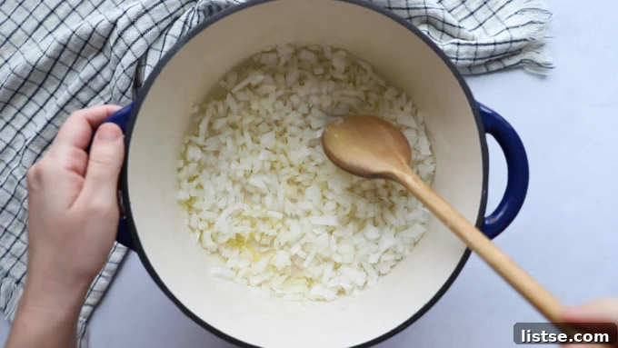Close-up shot of chopped onions being sautéed in a large Dutch oven with a hint of oil, forming the aromatic base for the chili.