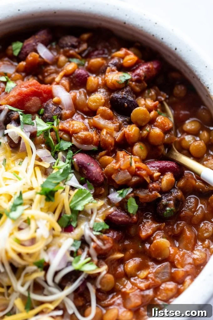 A steaming bowl of vegetarian chili, elegantly served with a spoon, highlighting its inviting texture and rich color.