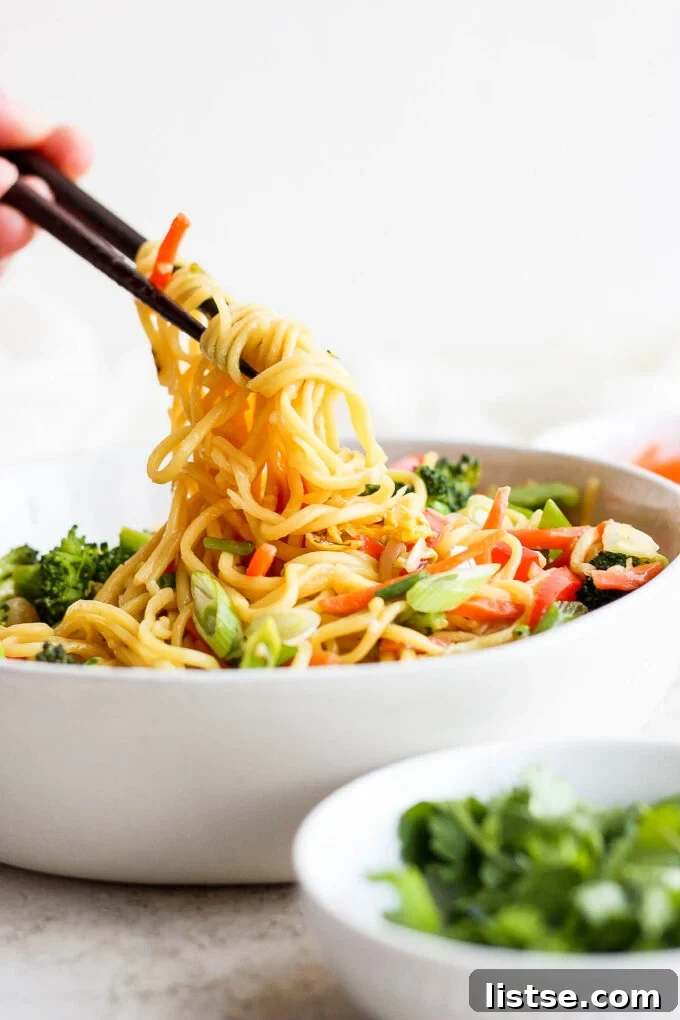 A close-up of vegetable chow mein in a large serving bowl, highlighting the colorful ingredients and savory sauce.