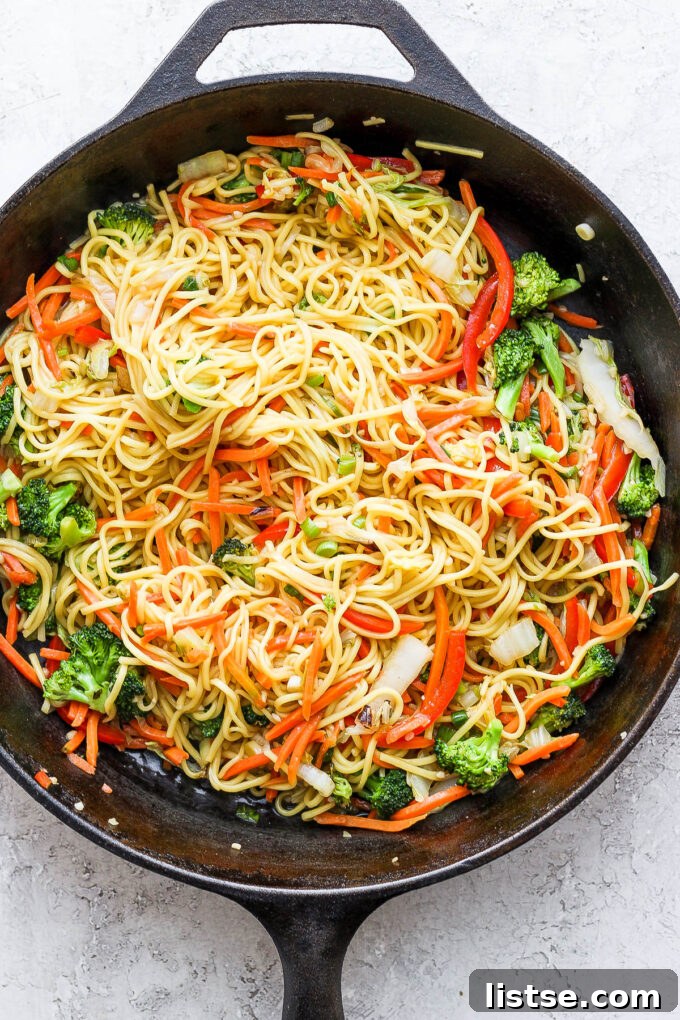 Final dish of vegetable chow mein in a cast iron skillet, garnished with fresh green onions.
