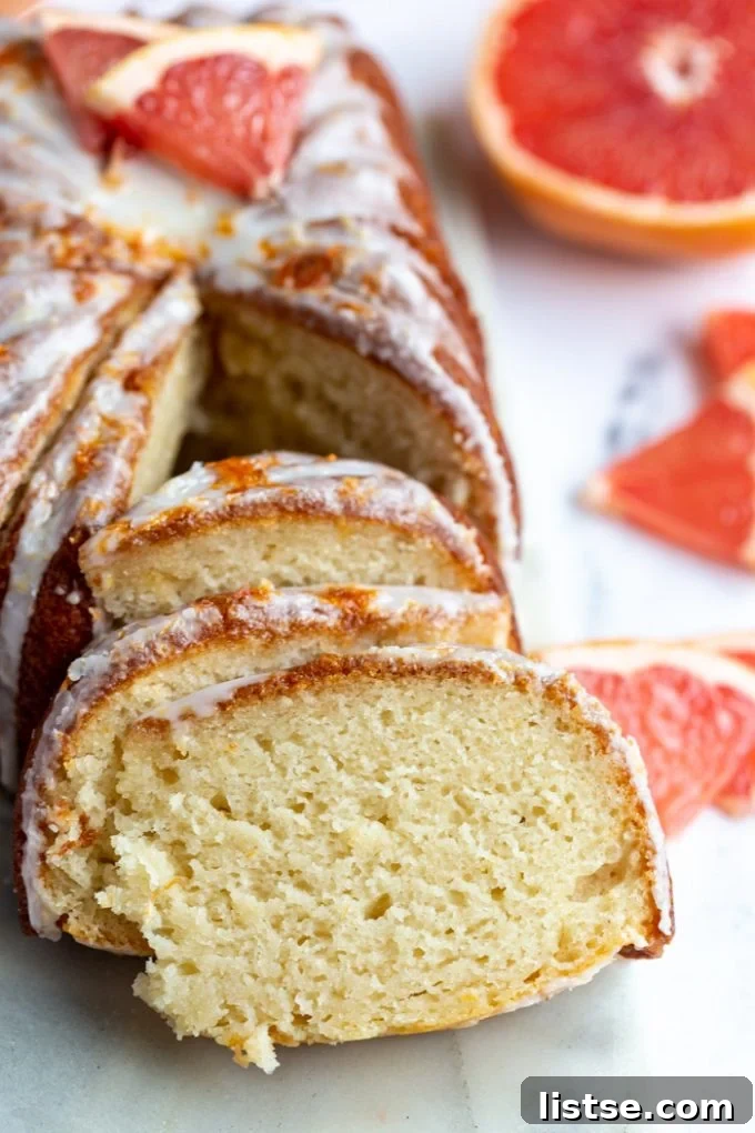 Zesty Vegan Grapefruit Loaf 3 grapefruit loaf cut into thin slices with the rest of the iced loaf in the background with fresh grapefruit slices