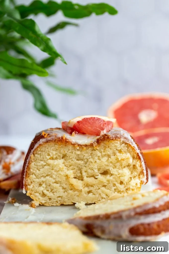 Zesty Vegan Grapefruit Loaf 4 grapefruit loaf cut in half with the rest of the iced loaf in the background with fresh grapefruit slices