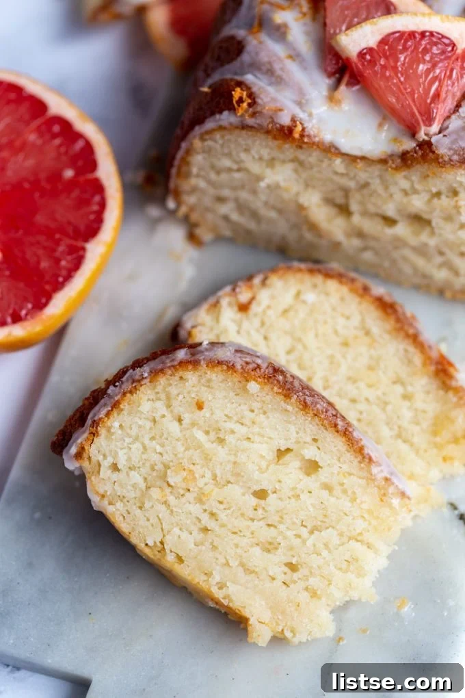 Zesty Vegan Grapefruit Loaf 5 grapefruit loaf cut into thin slices with the rest of the iced loaf in the background with fresh grapefruit slices
