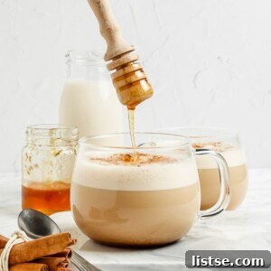 clear mug with a foamed latte in it. a hand drizzling honey on top into the mug