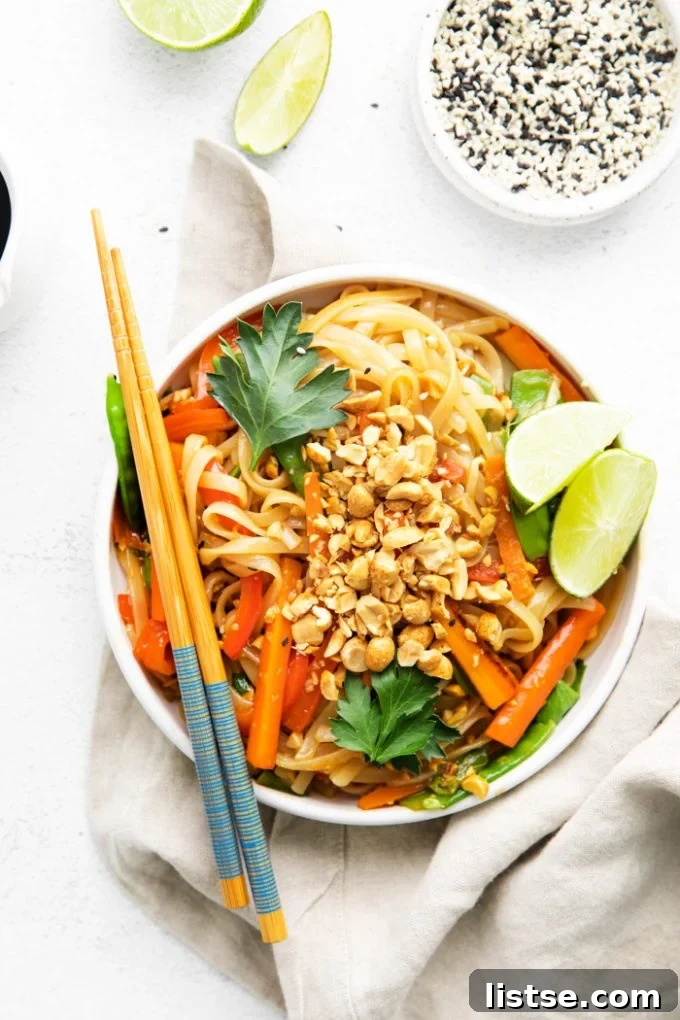 Close-up of vegan Pad Thai served in a white bowl with chopsticks, garnished with fresh lime and peanuts