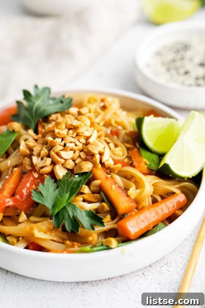 A beautifully plated vegan Pad Thai in a white bowl, garnished with chopped peanuts and lime wedges