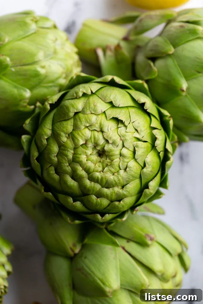 A stack of three fresh, vibrant green artichokes, showcasing their natural beauty and readiness for cooking.