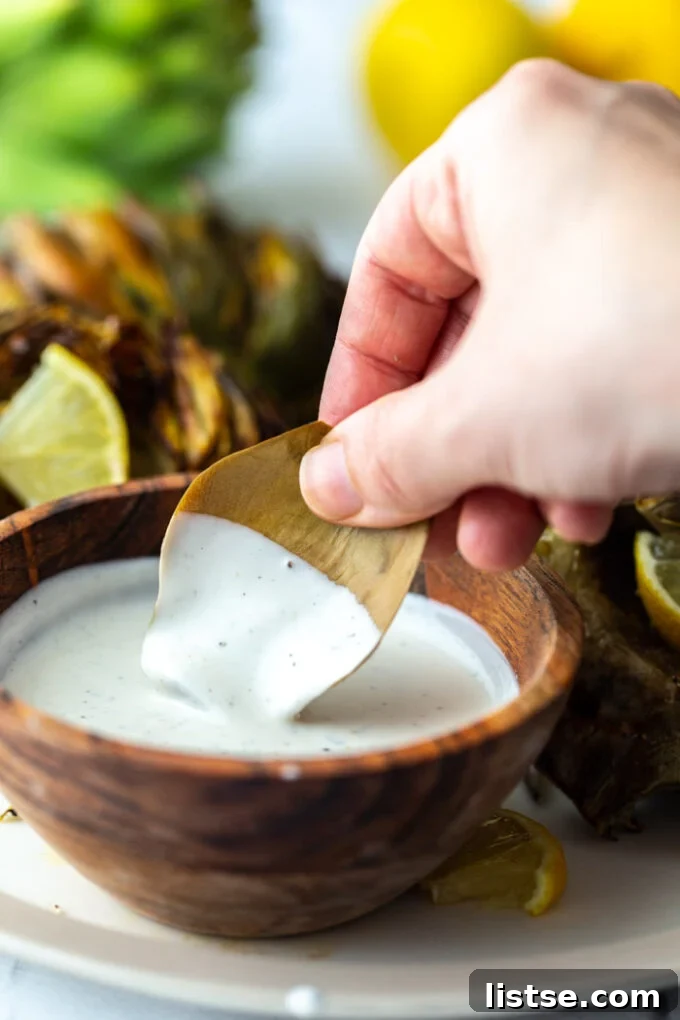 A person dipping a cooked artichoke leaf into a creamy white sauce, highlighting the delicious interaction.