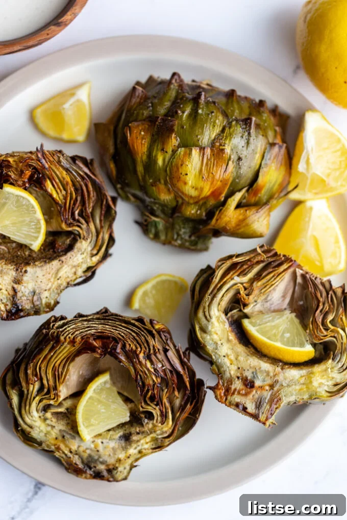 Four air-fried artichoke halves beautifully arranged on a white plate, with lemon slices and a focus on their crispy edges.